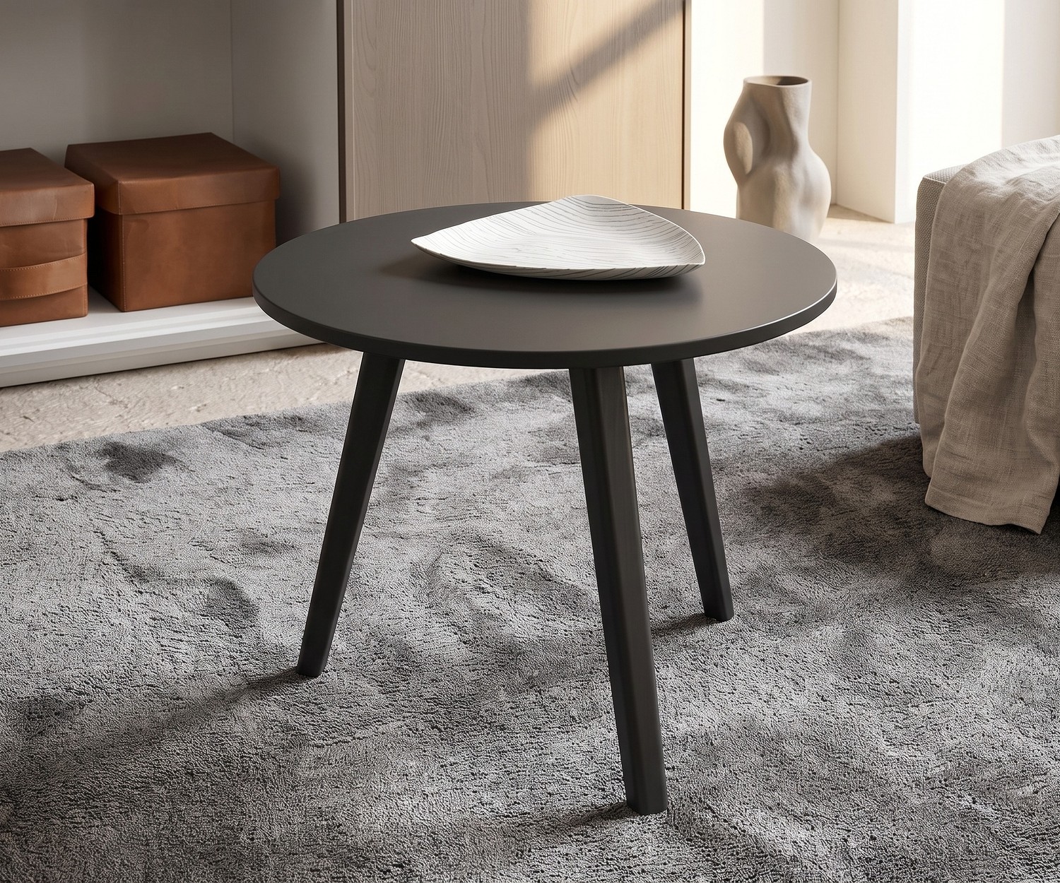 Tavolino da salotto Trio di Novamobili. Tavolino rotondo grigio scuro di design con tre gambe in legno su tappeto grigio.
