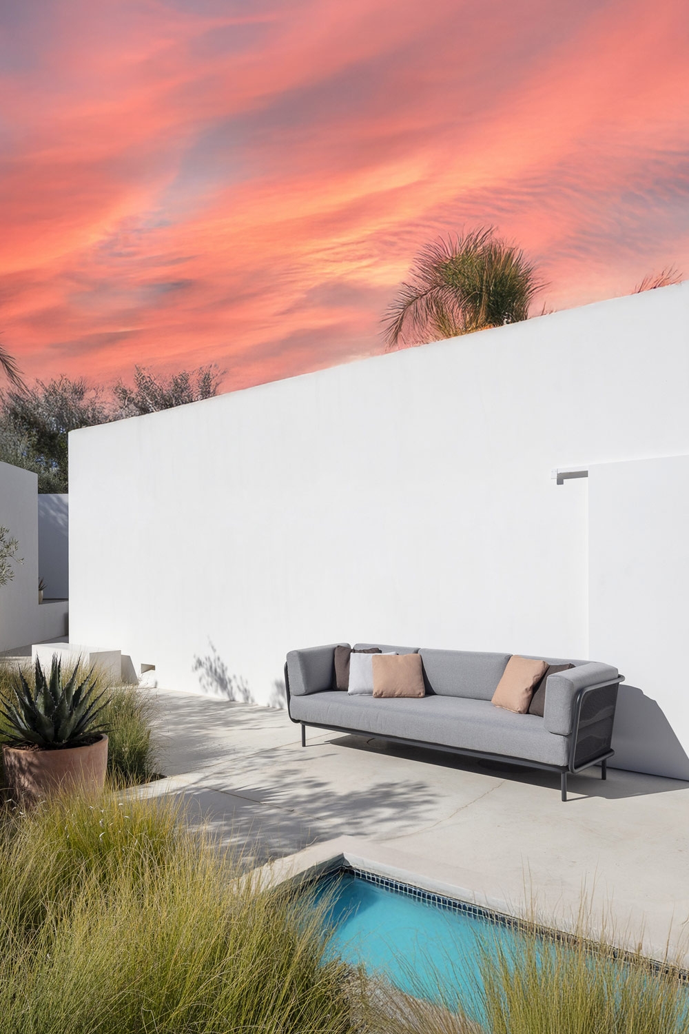 divano comfort dal design minimalista con cuscini schienale rotondi su una terrazza arredata in stile mediterraneo con piscina
