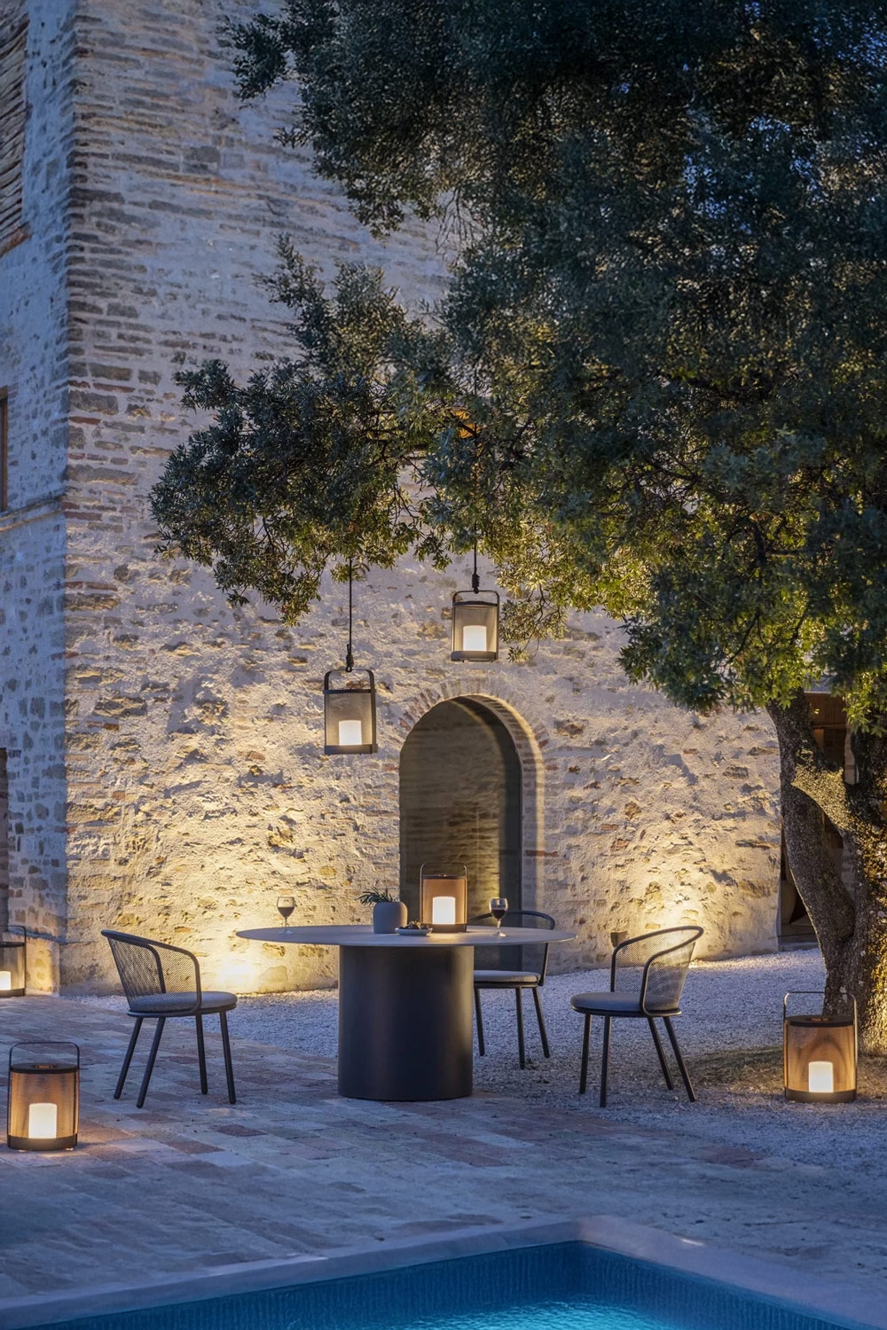 terrazza illuminata in modo suggestivo con tavolo moderno in acciaio inossidabile e ceramica e sedie da giardino in acciaio inossidabile