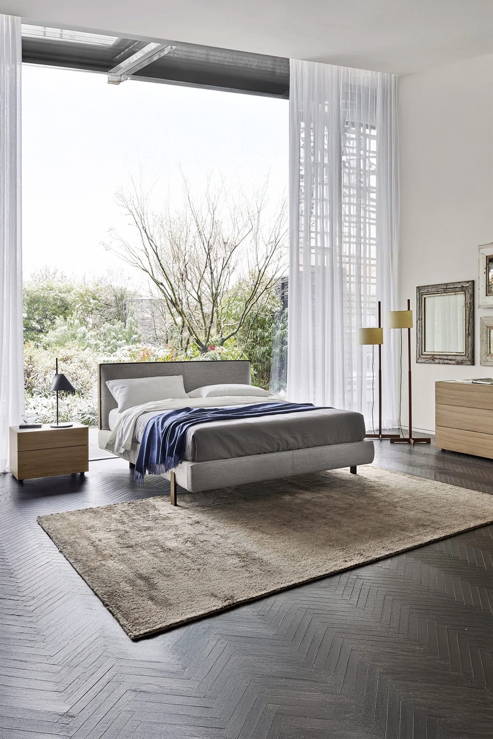 letto con cornice sottile con effetto sospeso e comodino senza maniglie davanti a una grande finestra