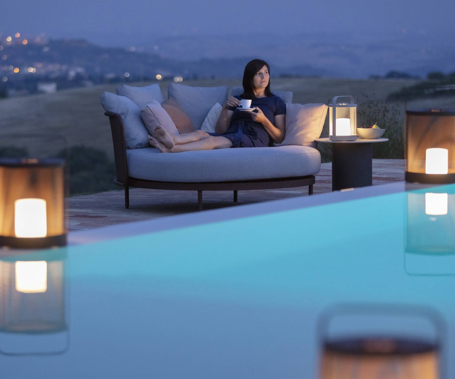 Atmosfera serale sulla terrazza della piscina con illuminazione e lettino Baza