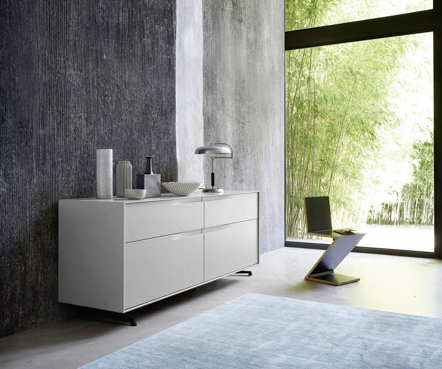 Cassettiera di design Vela laccata grigio opaco in camera da letto di fronte alla finestra frontale Cassettiera di design Vela laccata grigio opaco in camera da letto di fronte alla finestra frontale