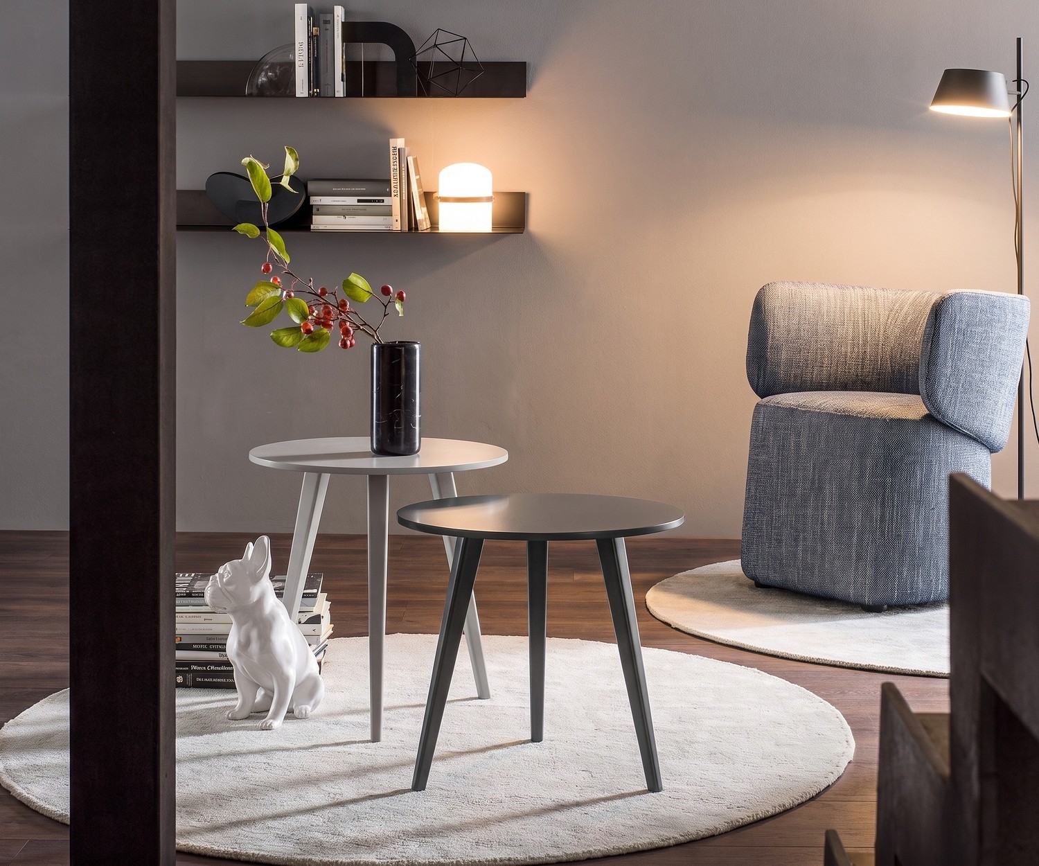 Tavolino di design Trio di Novamobili in soggiorno, moderni tavolini a tre gambe grigi in legno su tappeto rotondo con poltrona.